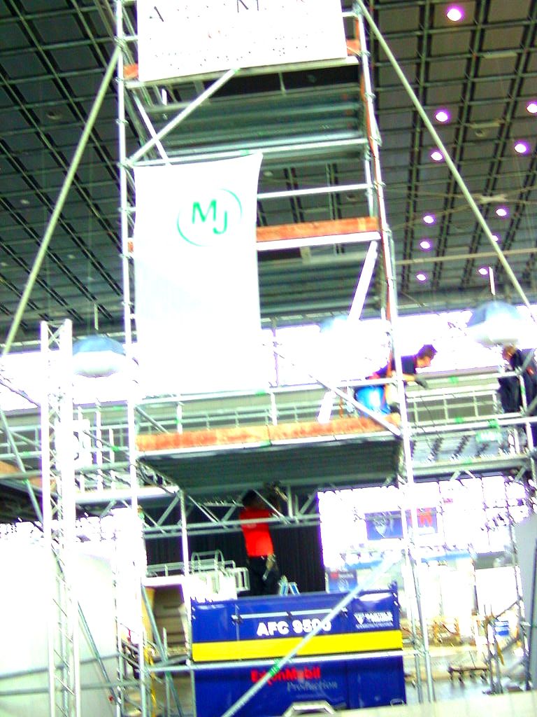 Gerüstturm in einer Messehalle, zwischen den Stielen hängt eine Bannerbahn mit rundem Zeichen