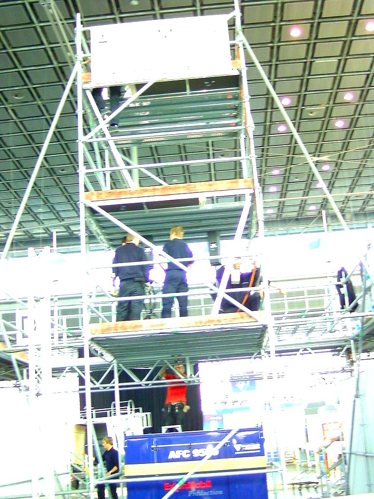 Hoher Gerüstturm in einer Messehalle, Monteure stehen auf dem Belag der mittleren Lage